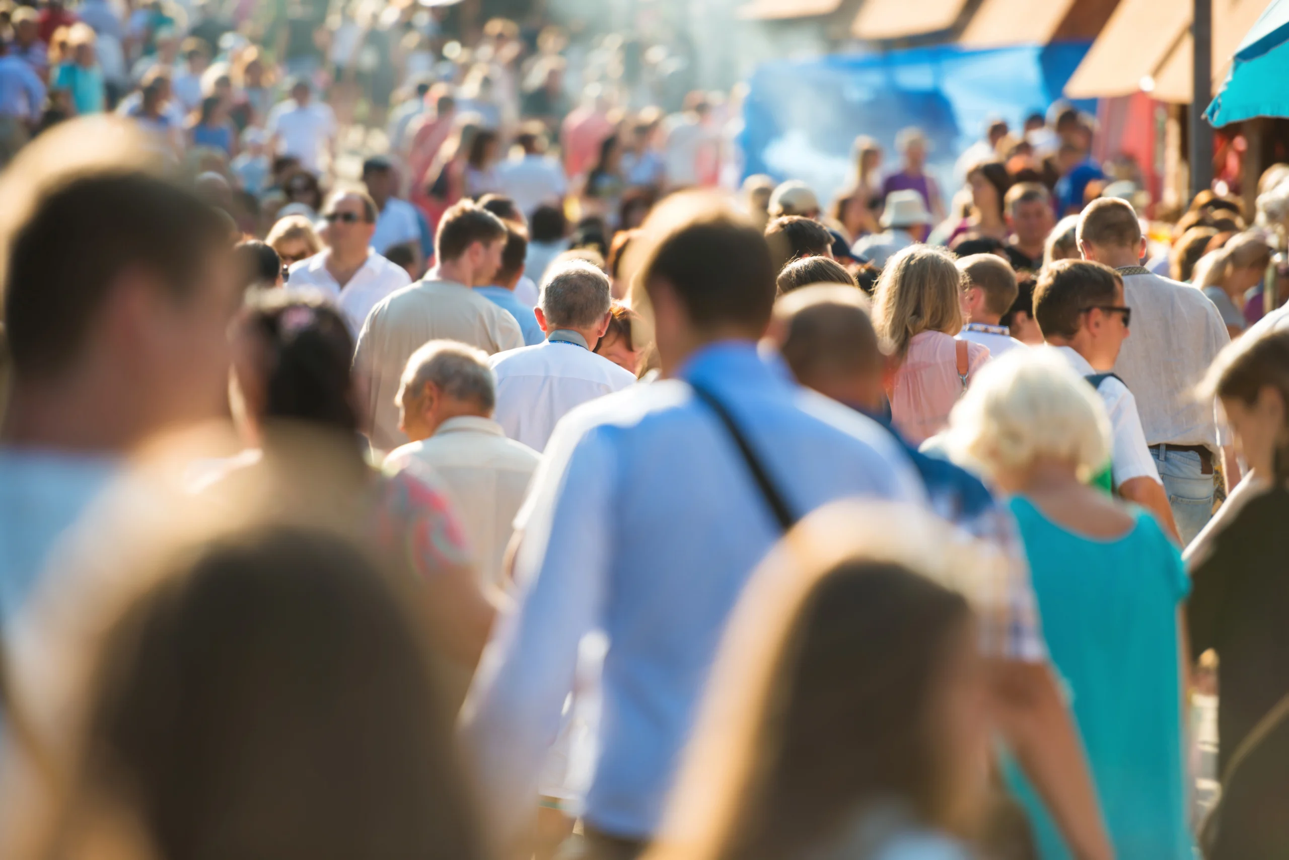 A crowd of people walking through a busy street during an event in the sun