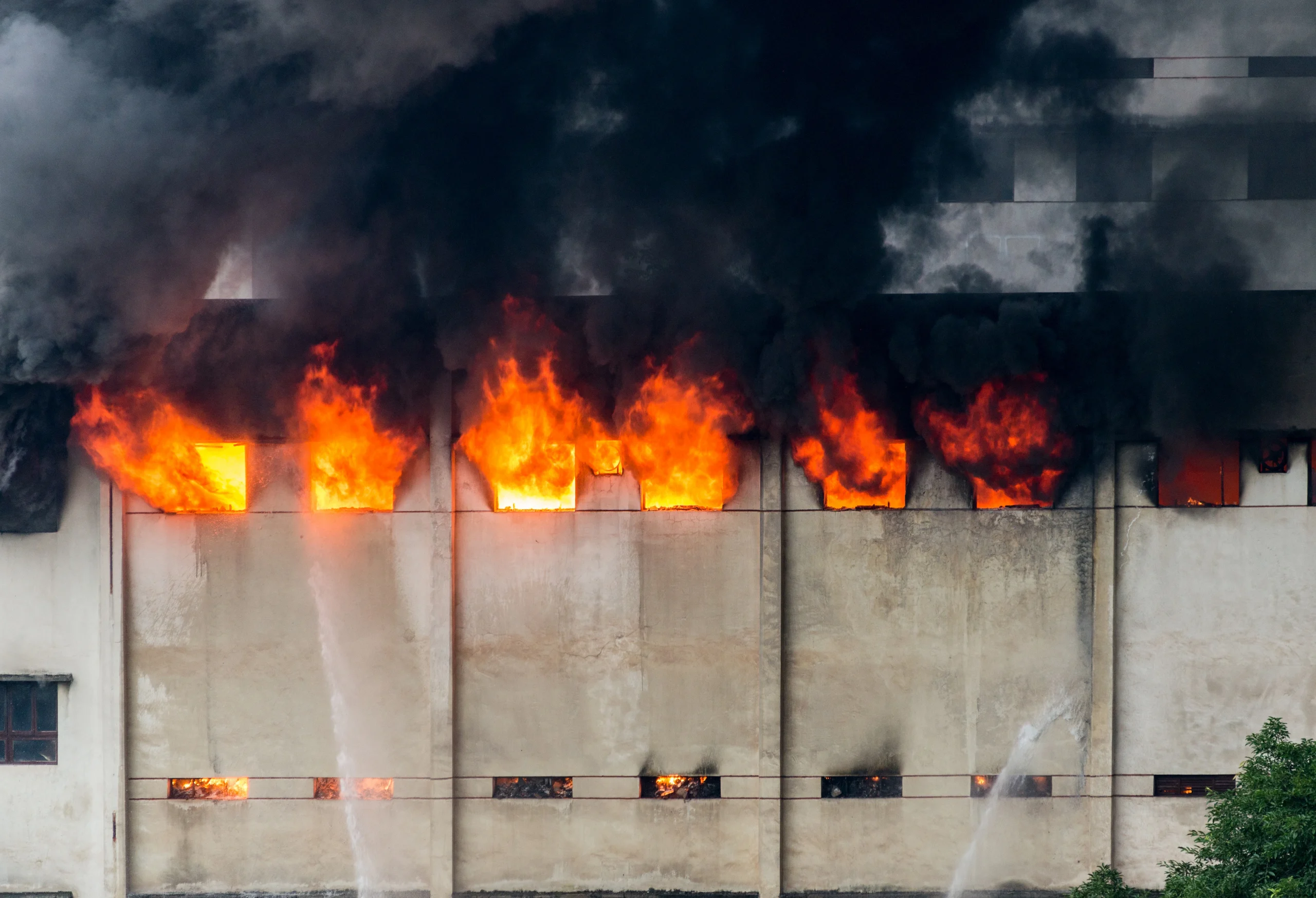 Photo of a fire in a factory during the day with big flames coming out of the building's windows