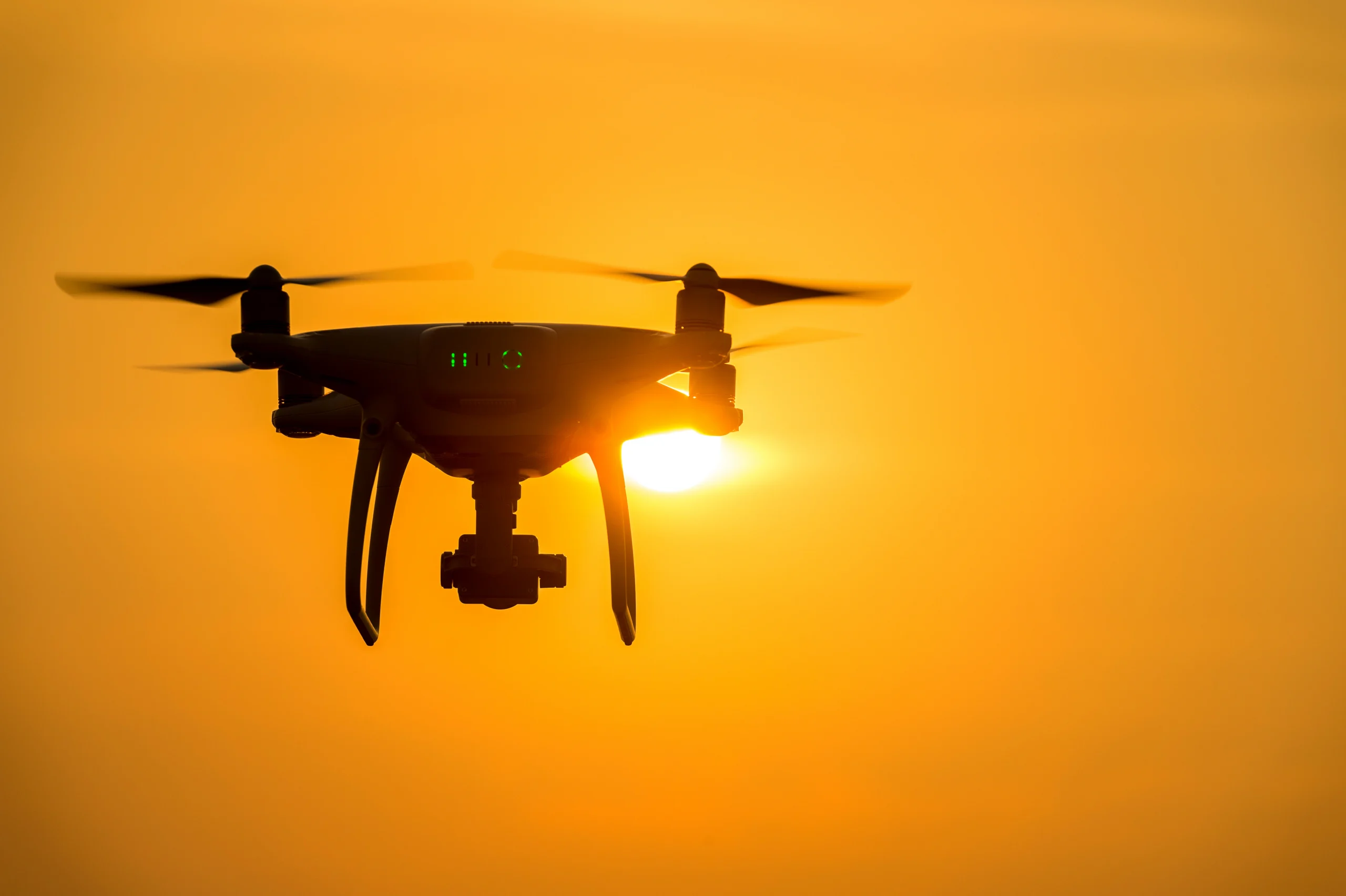 Drone flying with orange sky background as sun sets in the distance