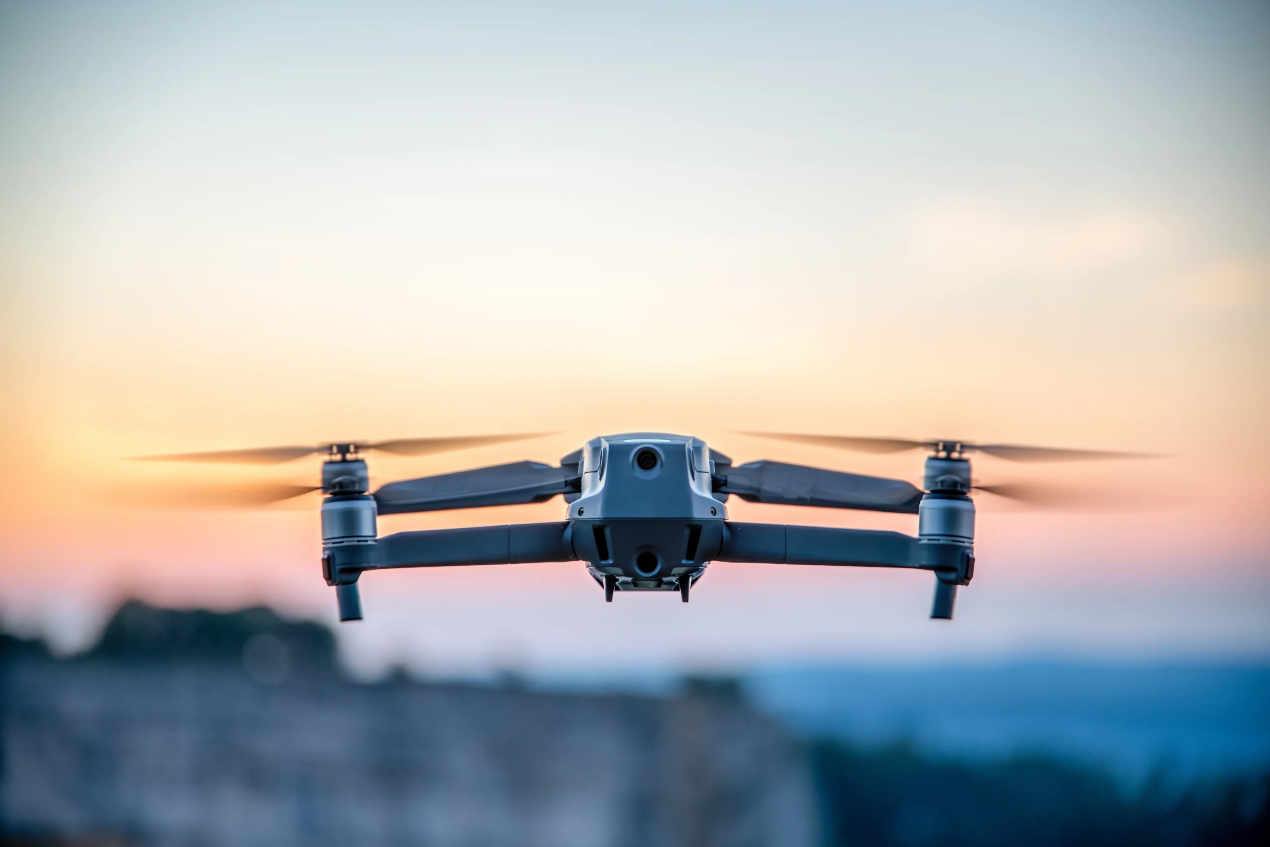 Autonomous security drone flying in the evening with orange and grey sky in background