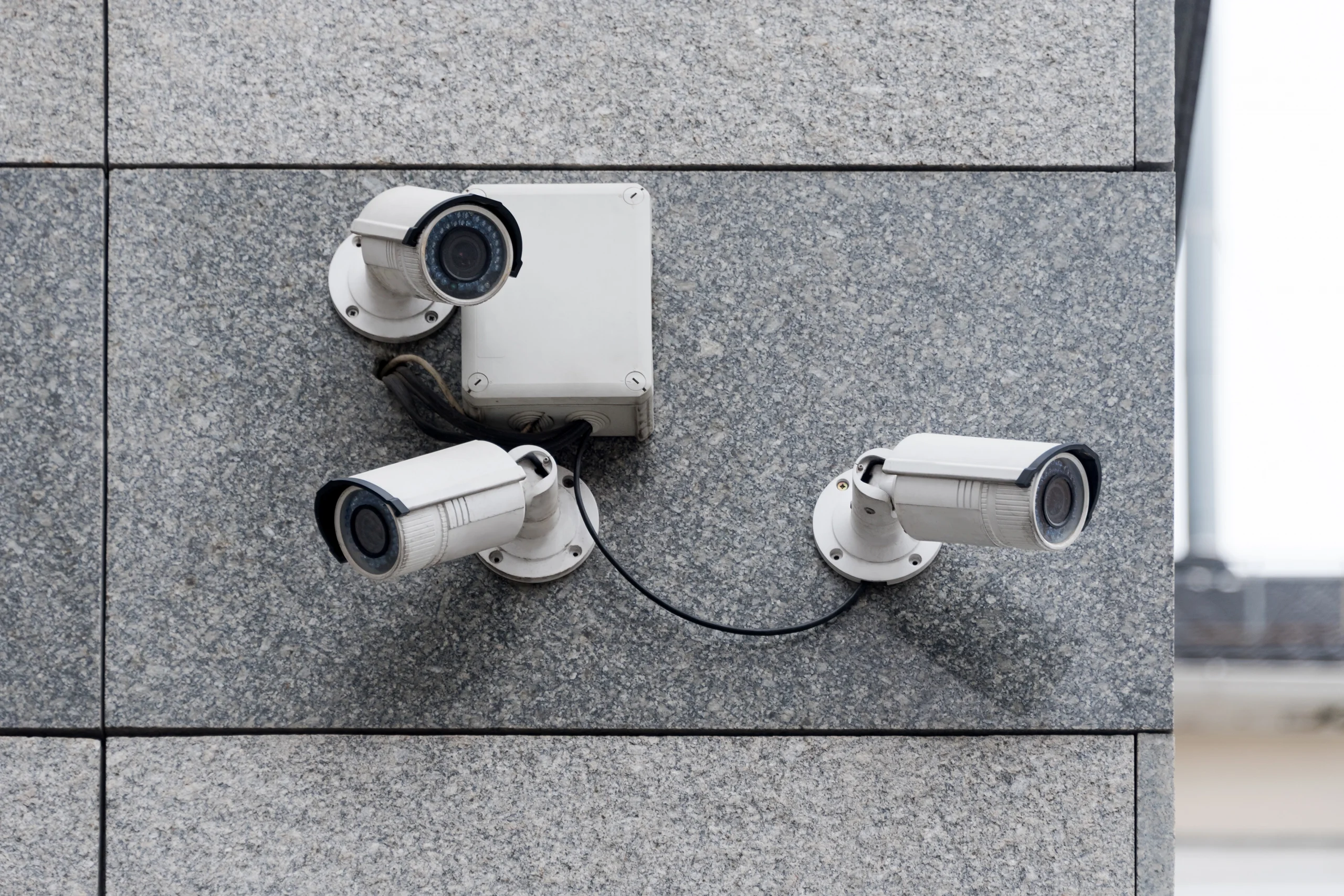 Multiple white security cameras facing different directions outside a grey building