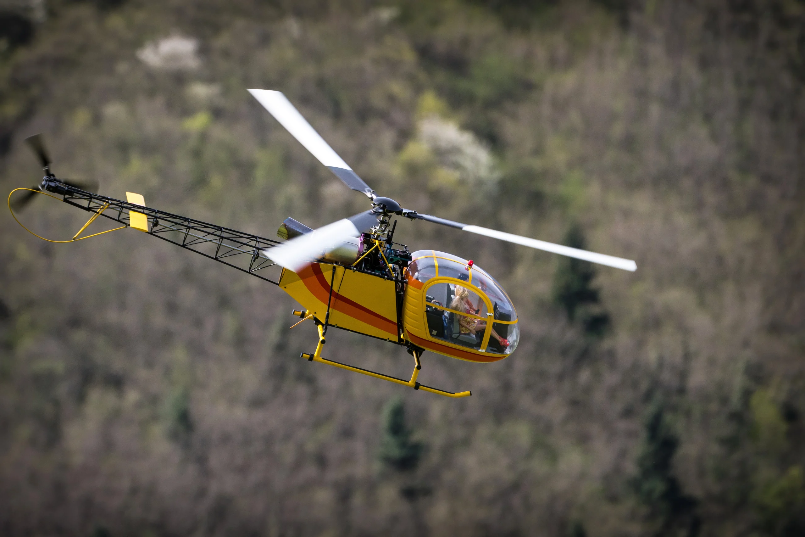 Yellow search and rescue helicopter with red stripe flying over a forest