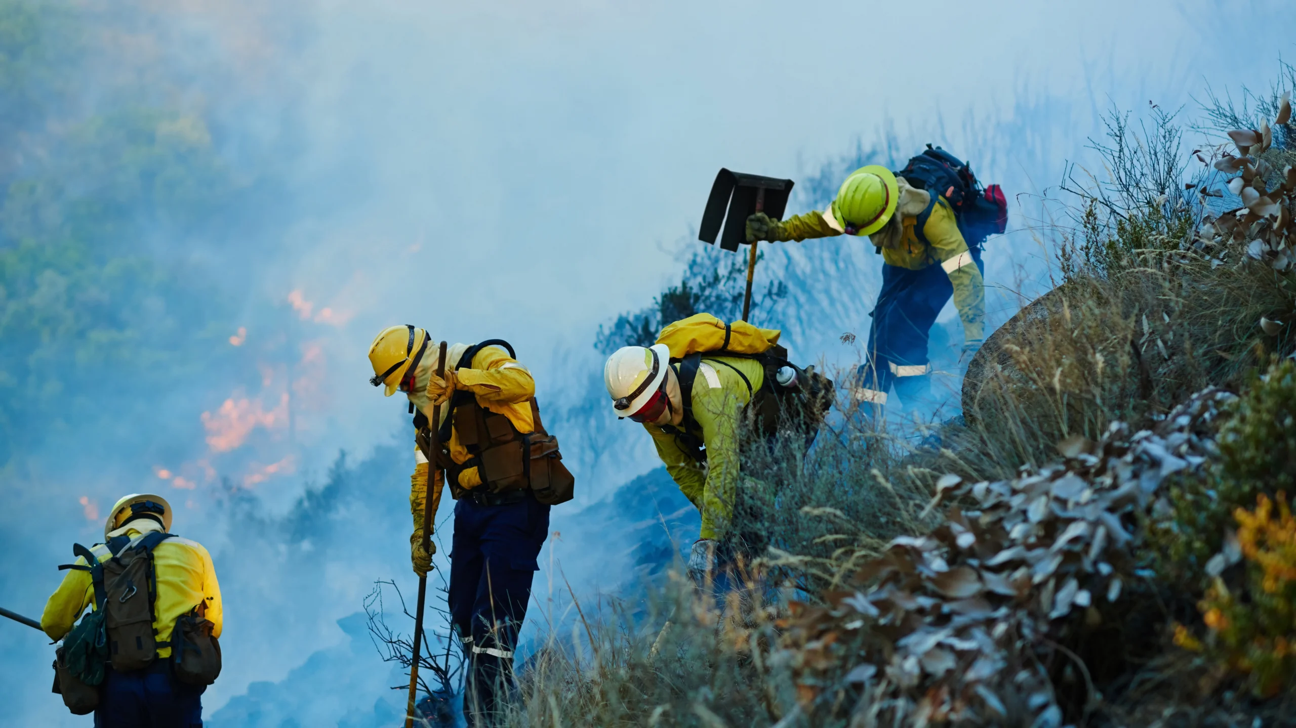 Search and rescue team searching on the side of a mountain with smoke and fire in the background